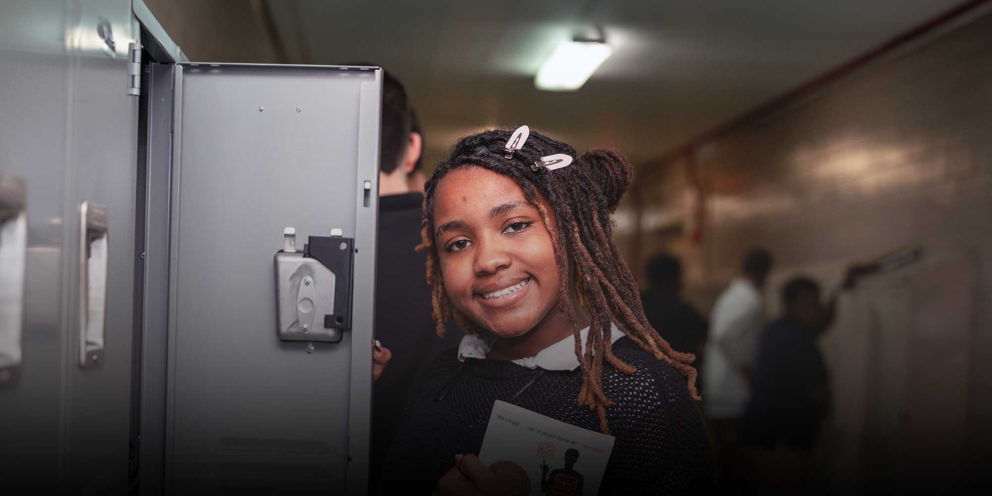 Smiling student standing by an open hallway locker.