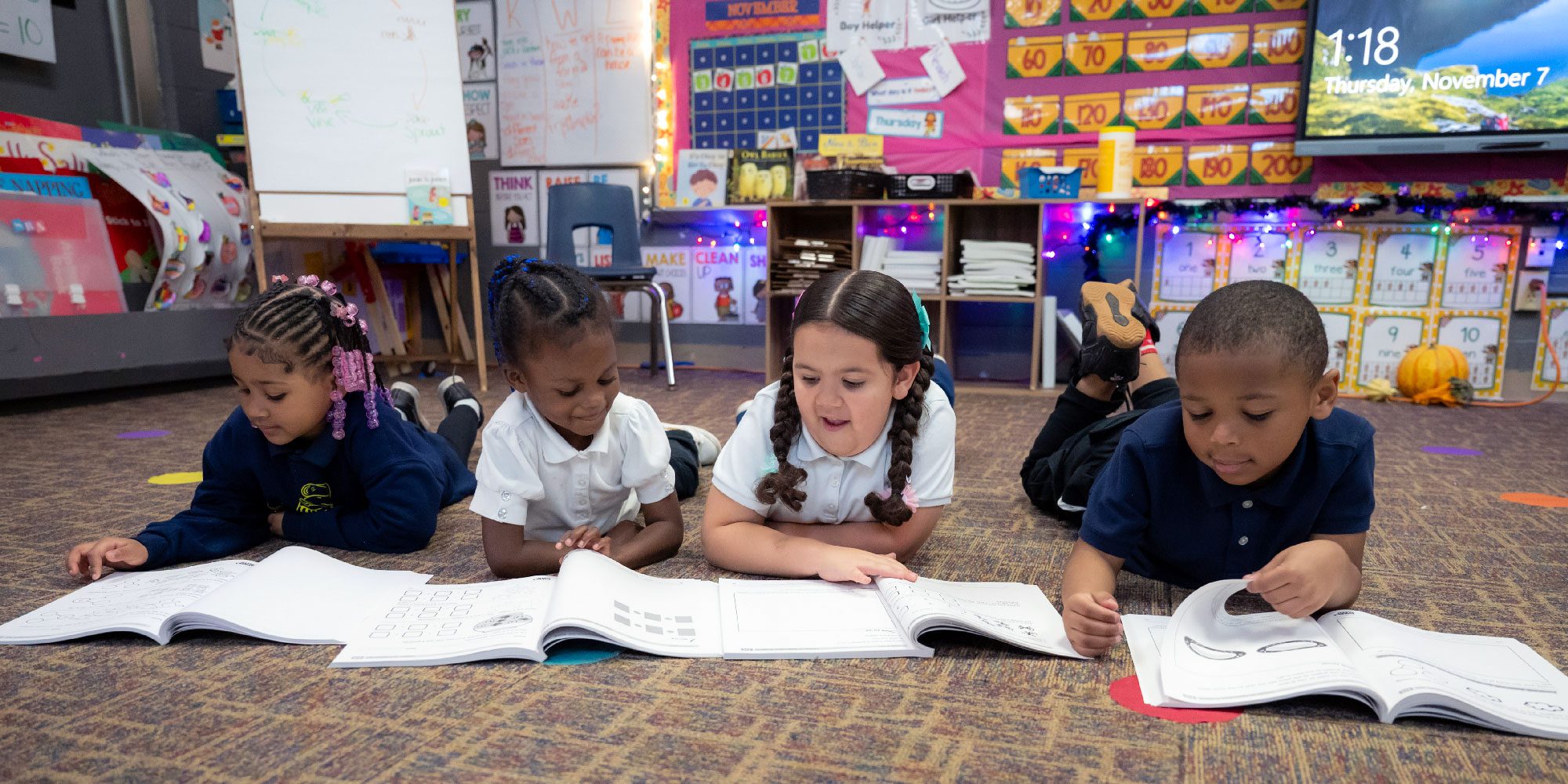 Four students reading books on a classroom floor.